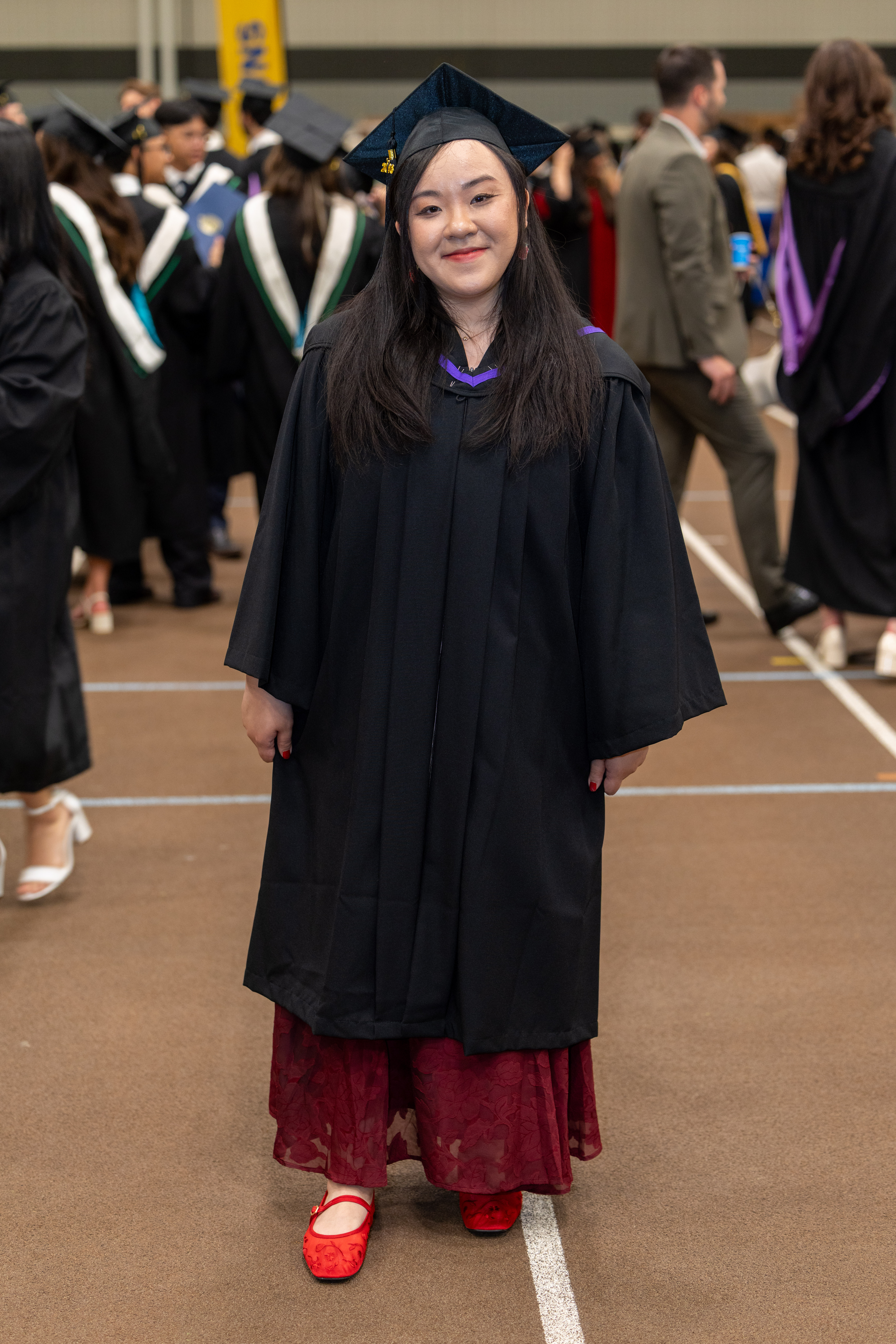 Kelena Van poses wearing her convocation cap and gown, with red shoes.