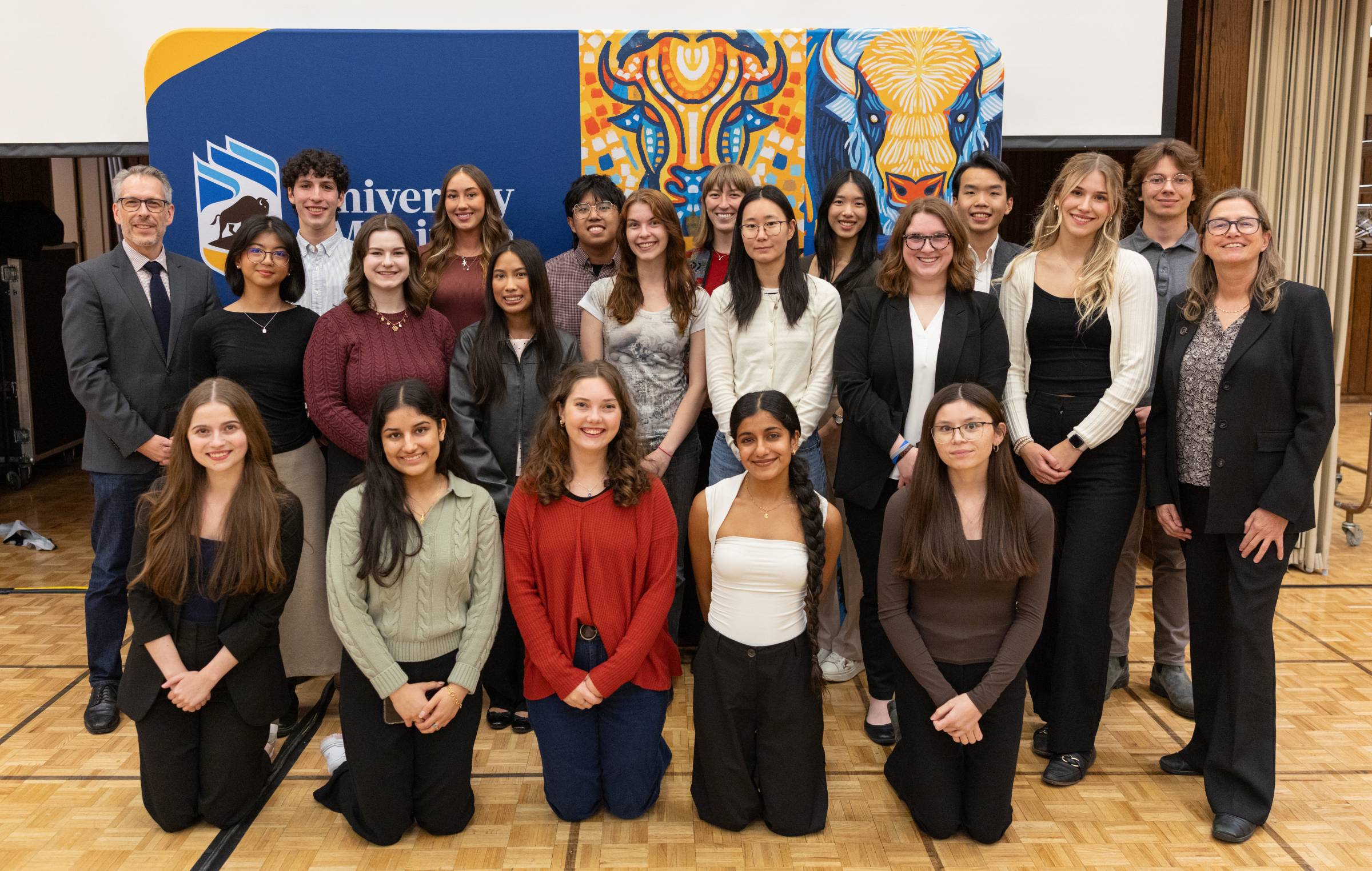Students pose together with faculty in front of a colourful bison-themed backdrop..