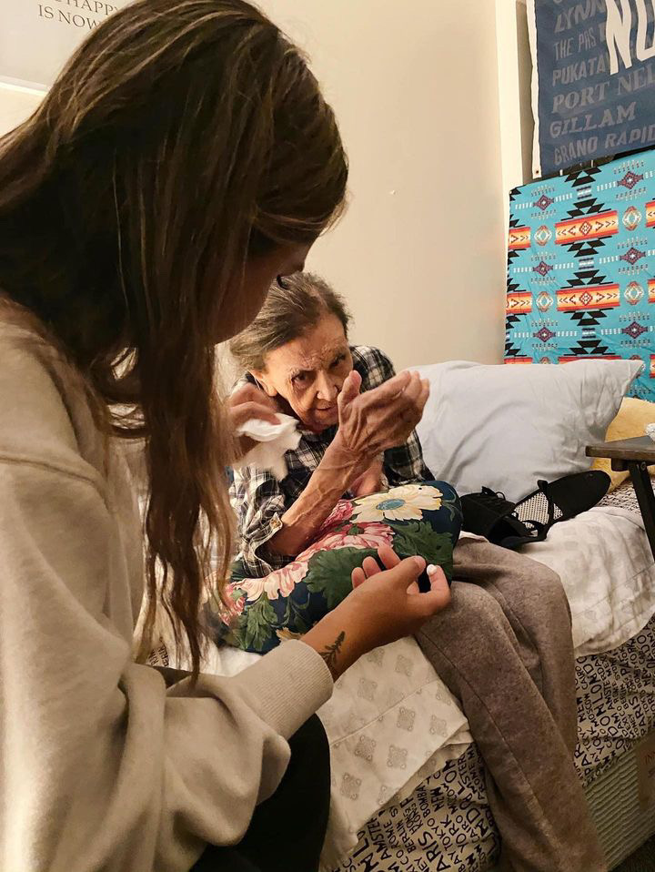 A young woman sits at her grandmother's bedside.