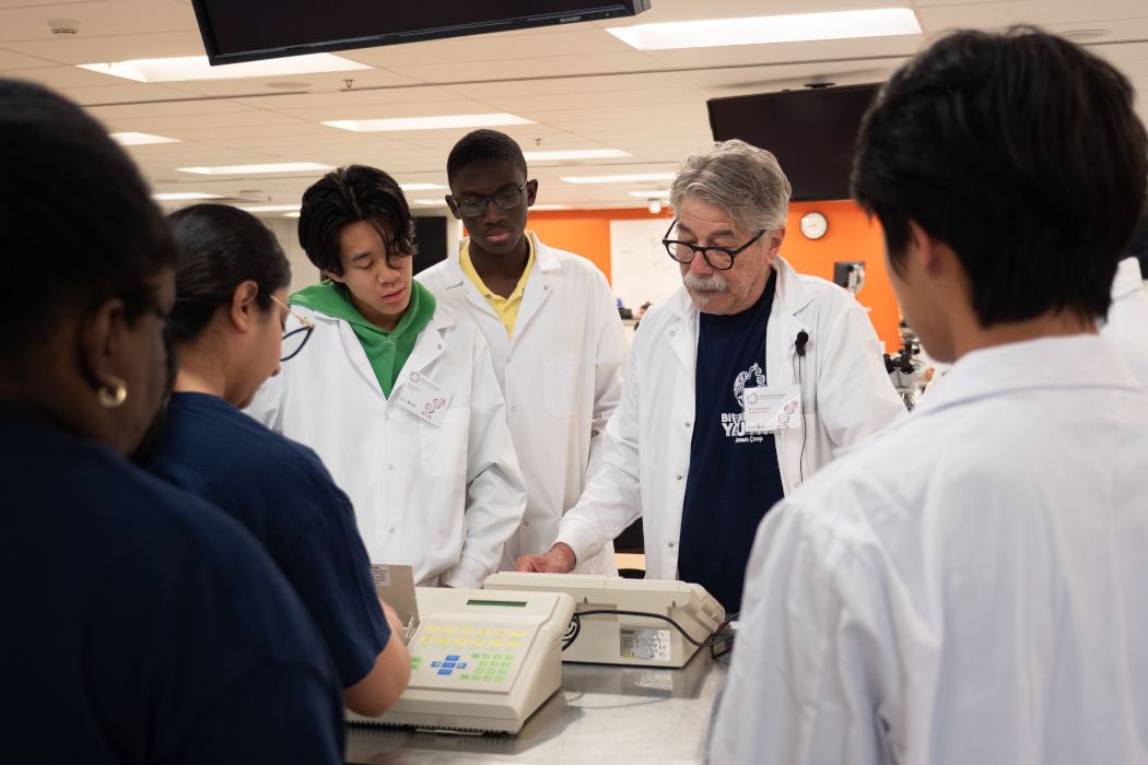 A group of students stand around a professor who is using a scientific device.