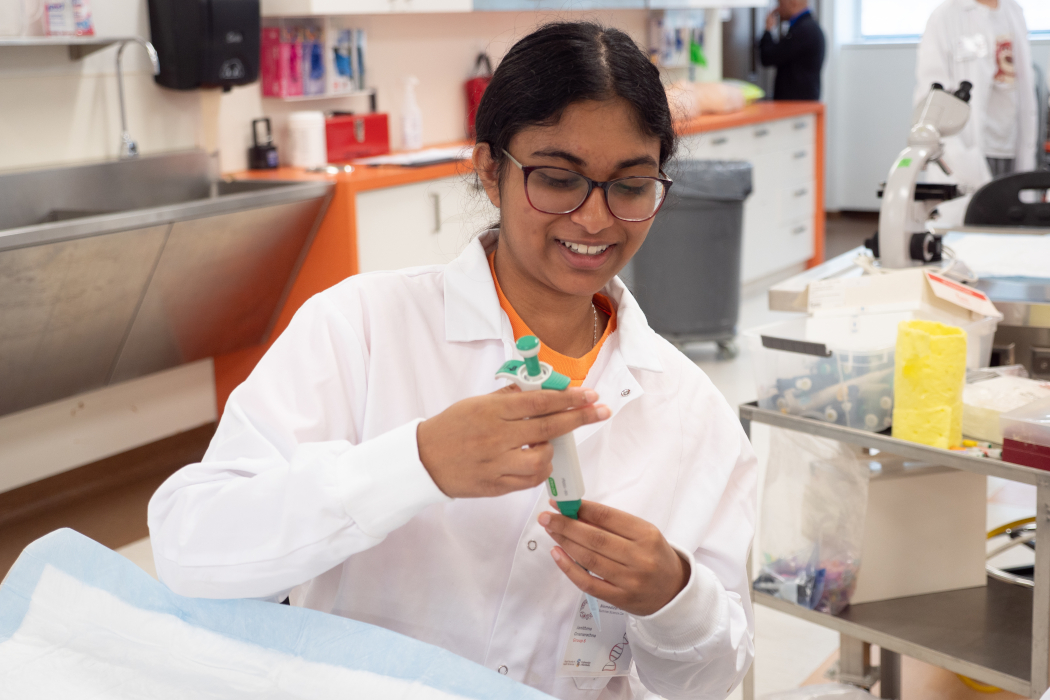 A student wearing a lab coat uses a pipette. 