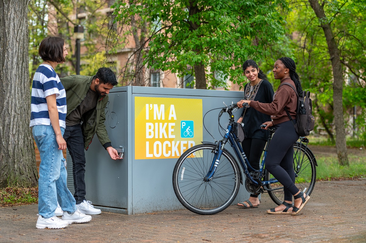 Individuals talk around a bike locker on campus.