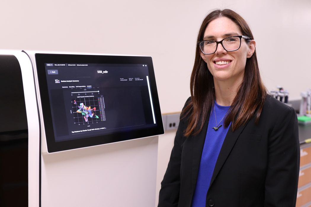 Dr. Britt Drögemöller stands in front of a large machine used in research.