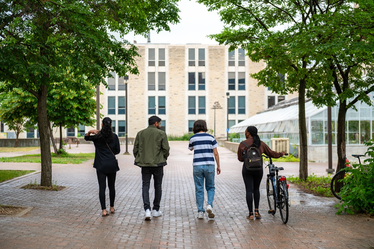 Four students walk towards Allen Building under the tree canopy.