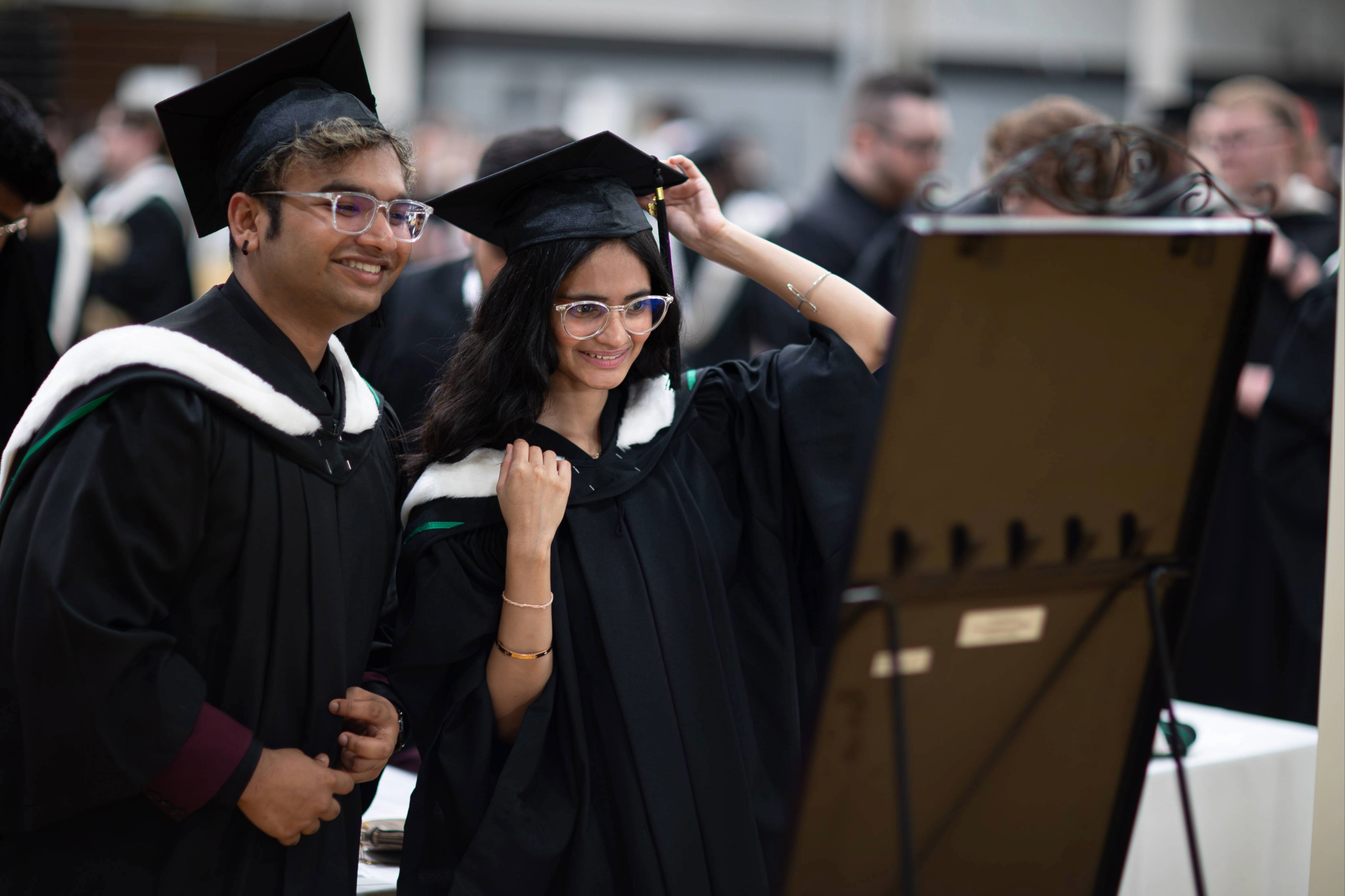 Two graduands looking in the mirror while getting ready at Convocation.