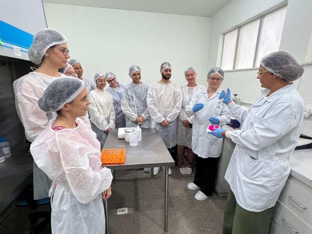 A group of students form a semicircle around two instructors in a lab.