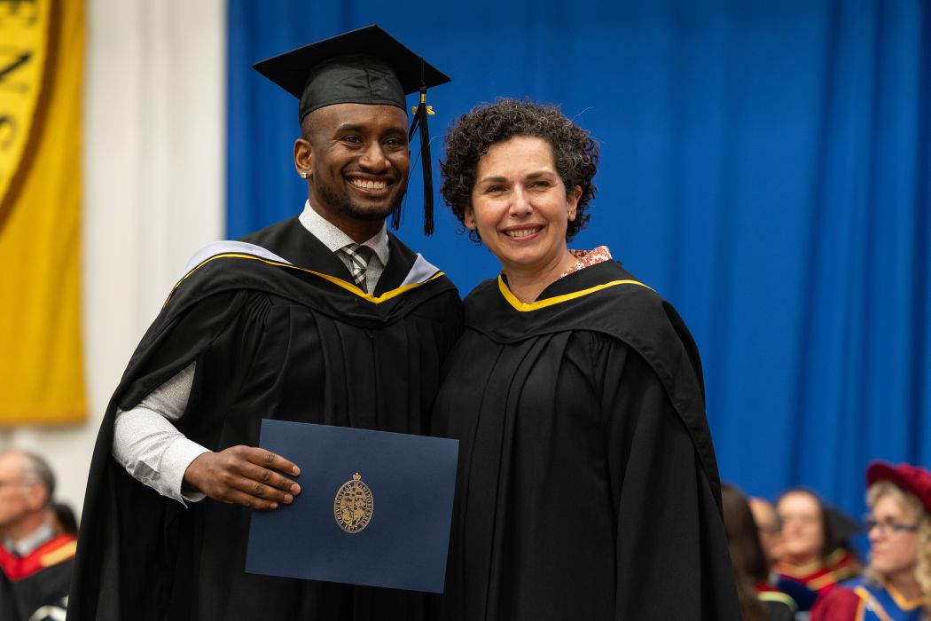 Dr. Terrell Okotcha wearing a cap and gown with Dr. Anastasia Kelekis-Cholakis on stage.