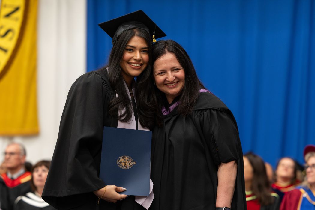 Jasleen Sanghera wears a graduation cap and gown with Mary Bertone on stage.