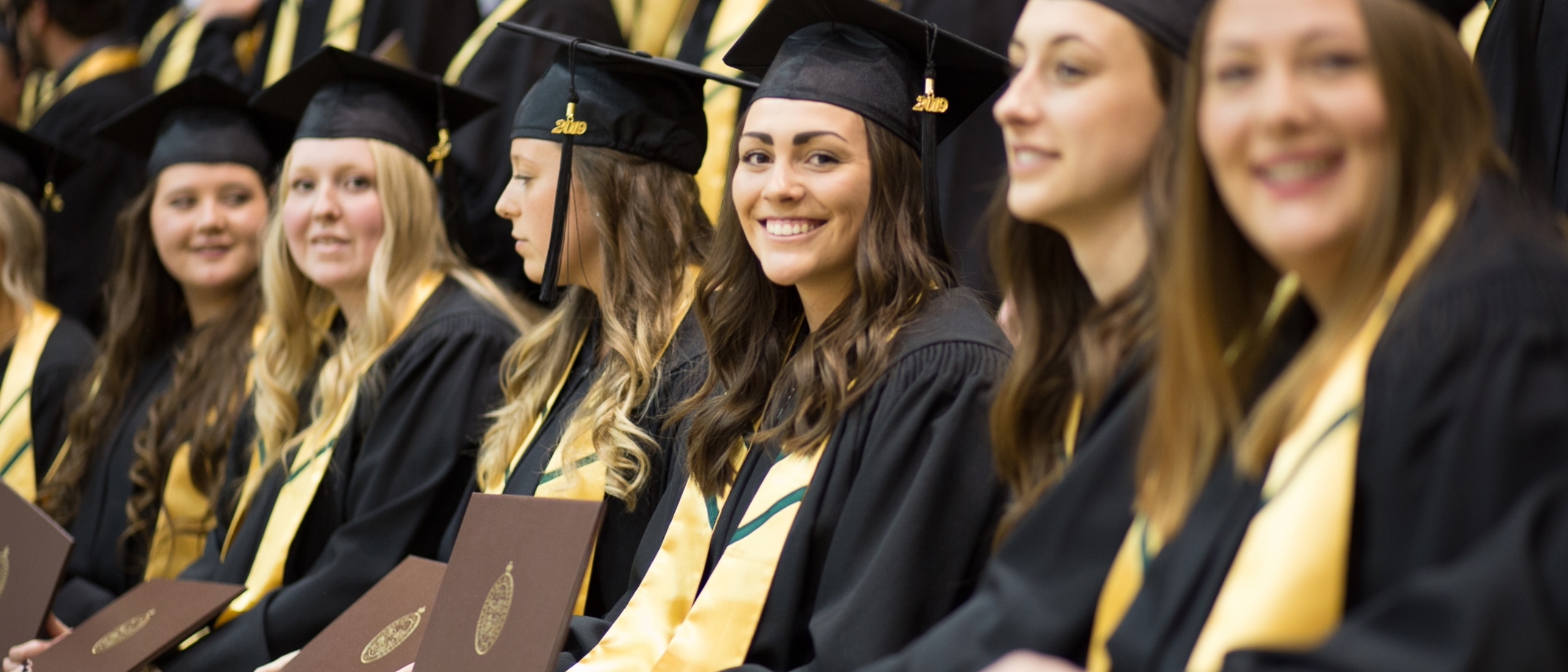 Row of smiling young women in UM cap and gown.