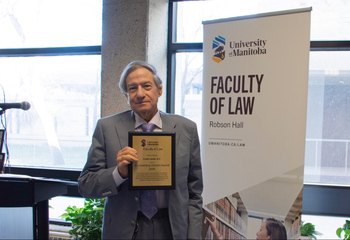 Frank Lavitt wears a grey suit and holds an outstanding alumni award brass plaque