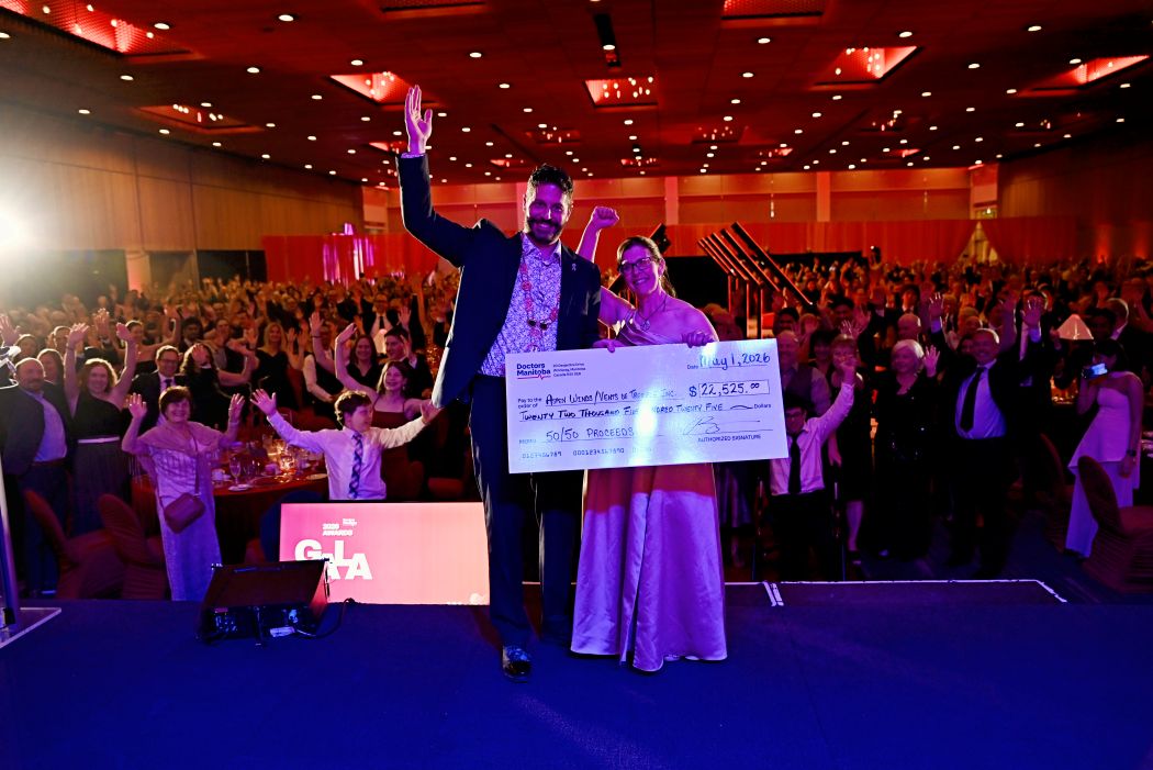 Two people hold a large cheque with a crowd behind them.