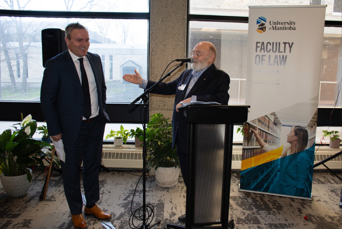 Evan Johnston laughs as Nick Slonosky leans on the podium gesturing towards him with praise and good humour.