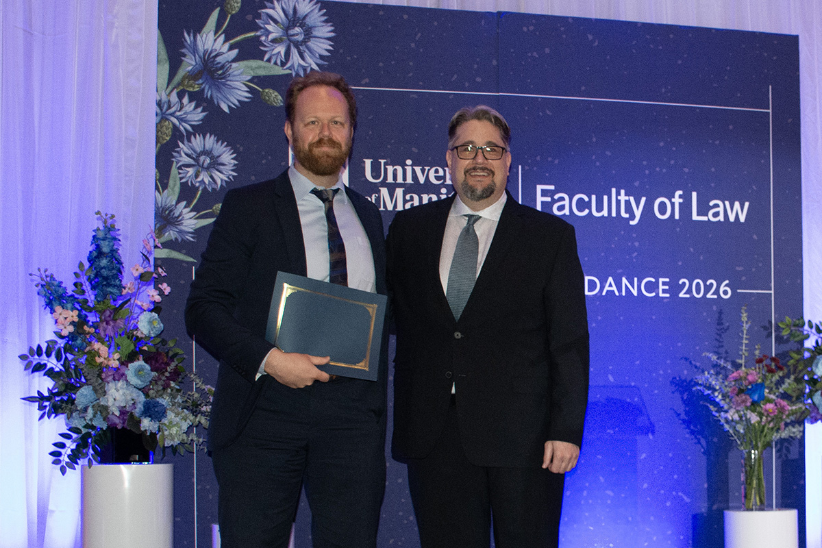two men in suits smile on a stage one hands the other an award certificate