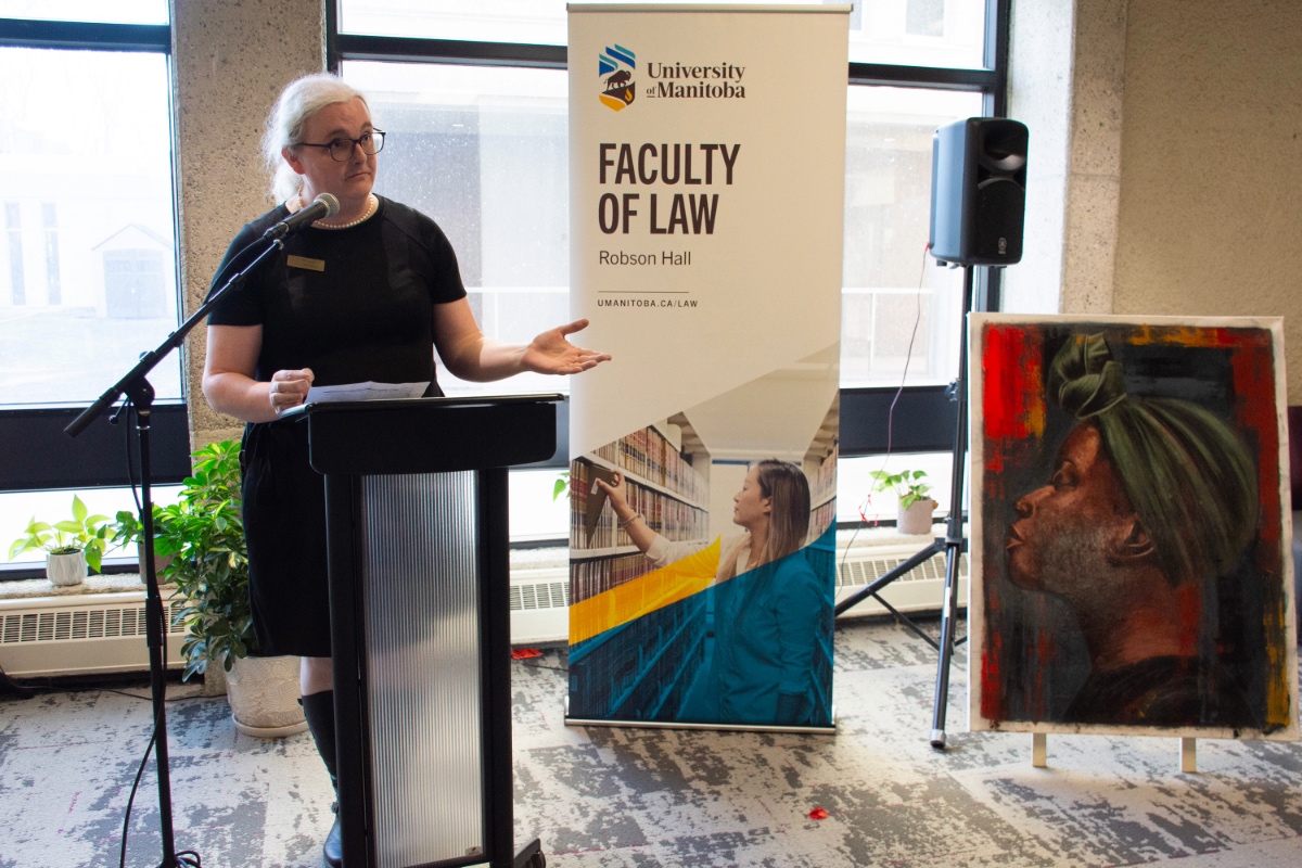 Lily Deardorff stands at a podium gesturing towards an oil painting mounted on an easel