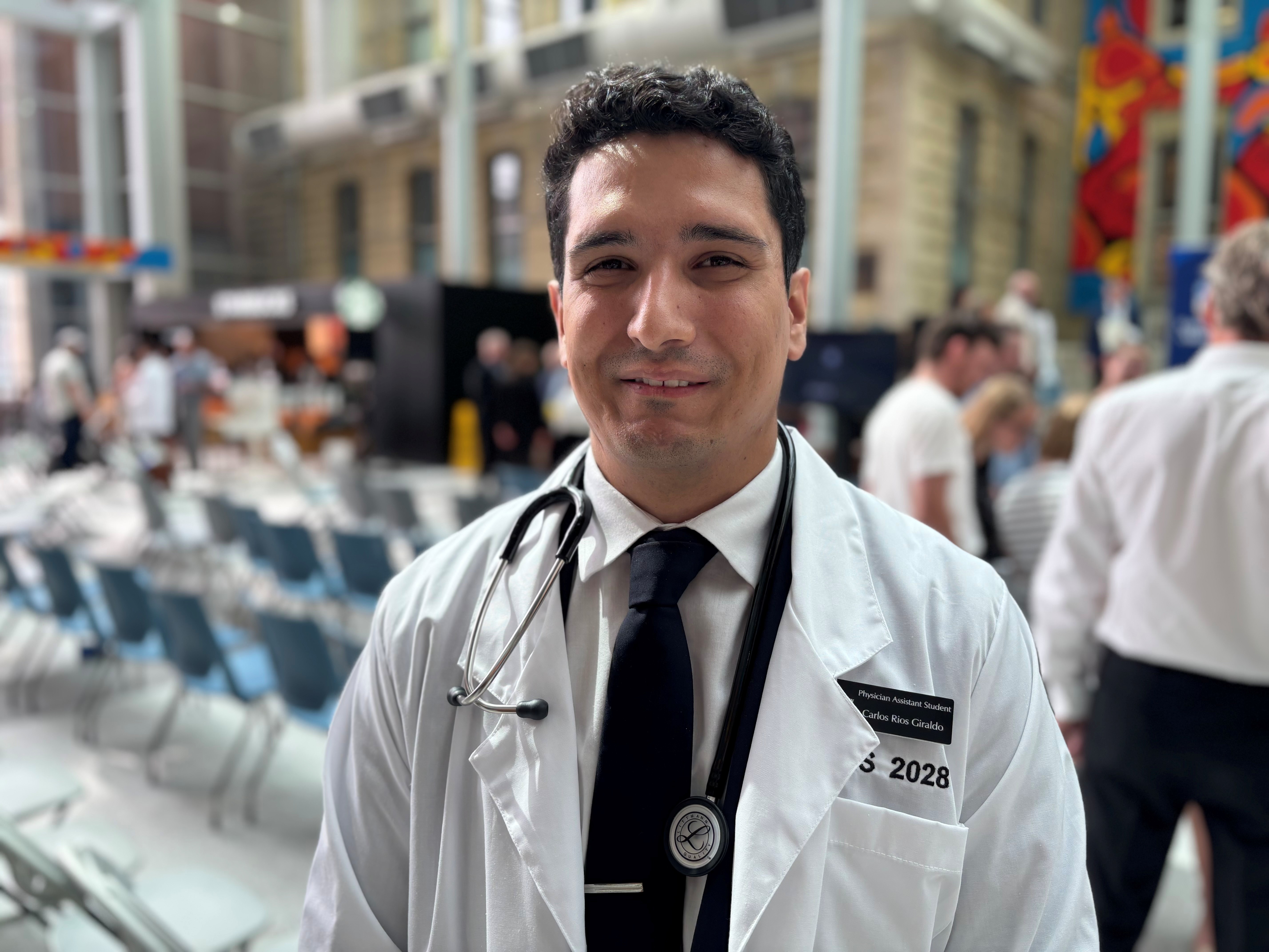 Portrait of Carlos Rios Giraldo wearing a white coat and a stethoscope around his neck. 