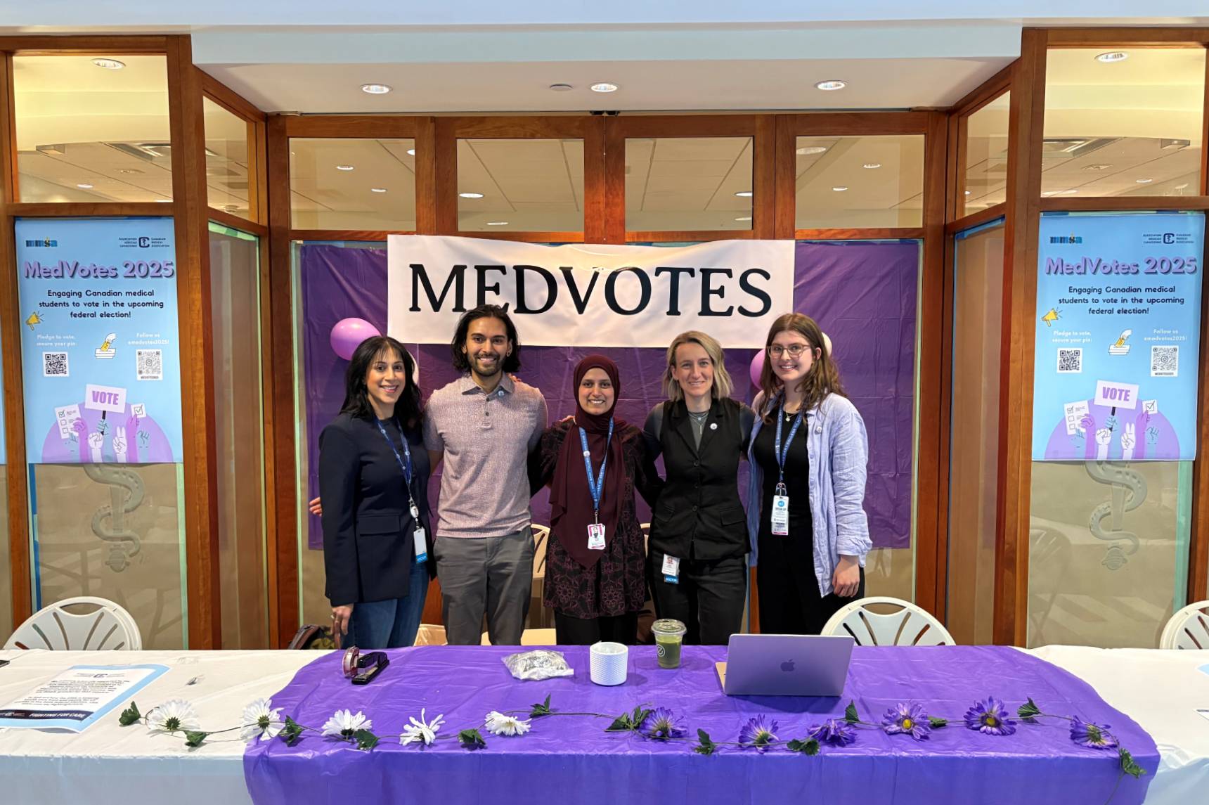 Five people smiling at the camera, standing behind a table at the MedVotes booth.