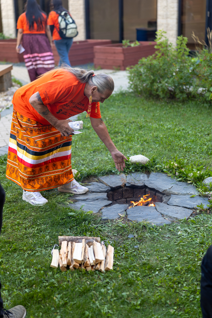 Elder Charlotte Nolin, dressed in orange, places tobacco into the fire at the Medicine Garden.