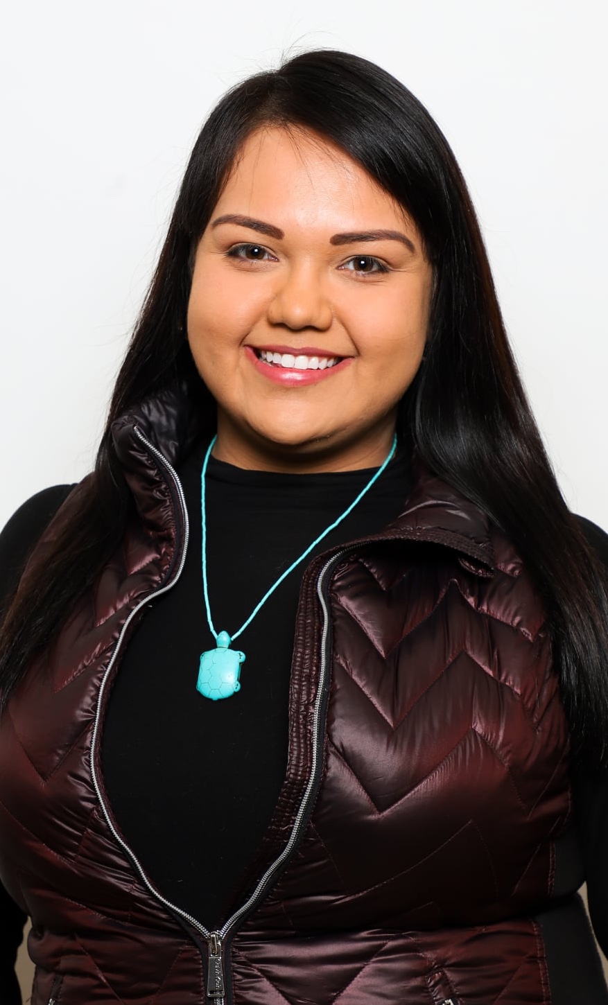 headshot of woman in leather vest and black top with blue turtle necklace