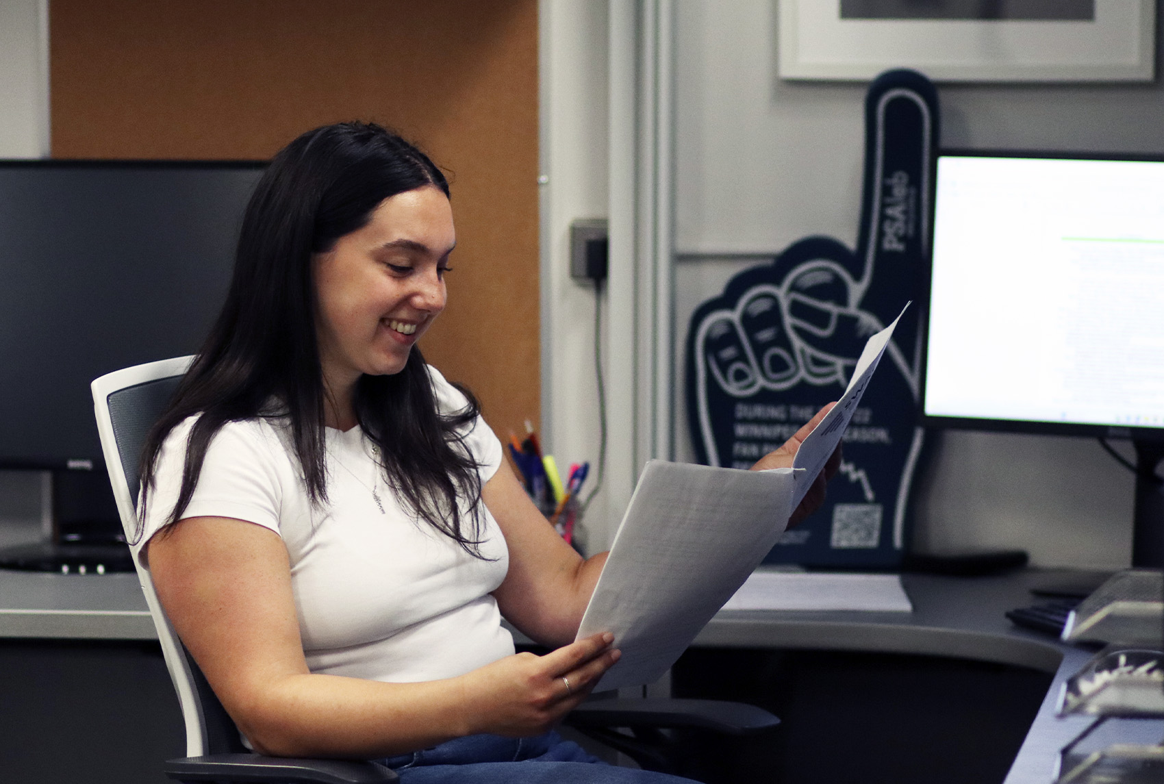 A young woman researcher sits in an office chair and flips through a research report.