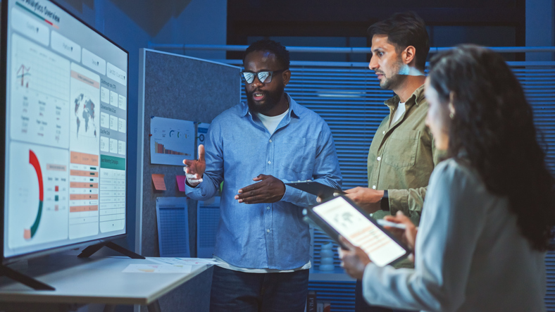 Three researchers studying and analyzing data in front of a screen in a lab setting.
