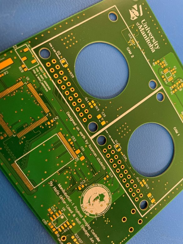 A green printed circuit board (part of CubeSat) with various electronic components and labels visible.