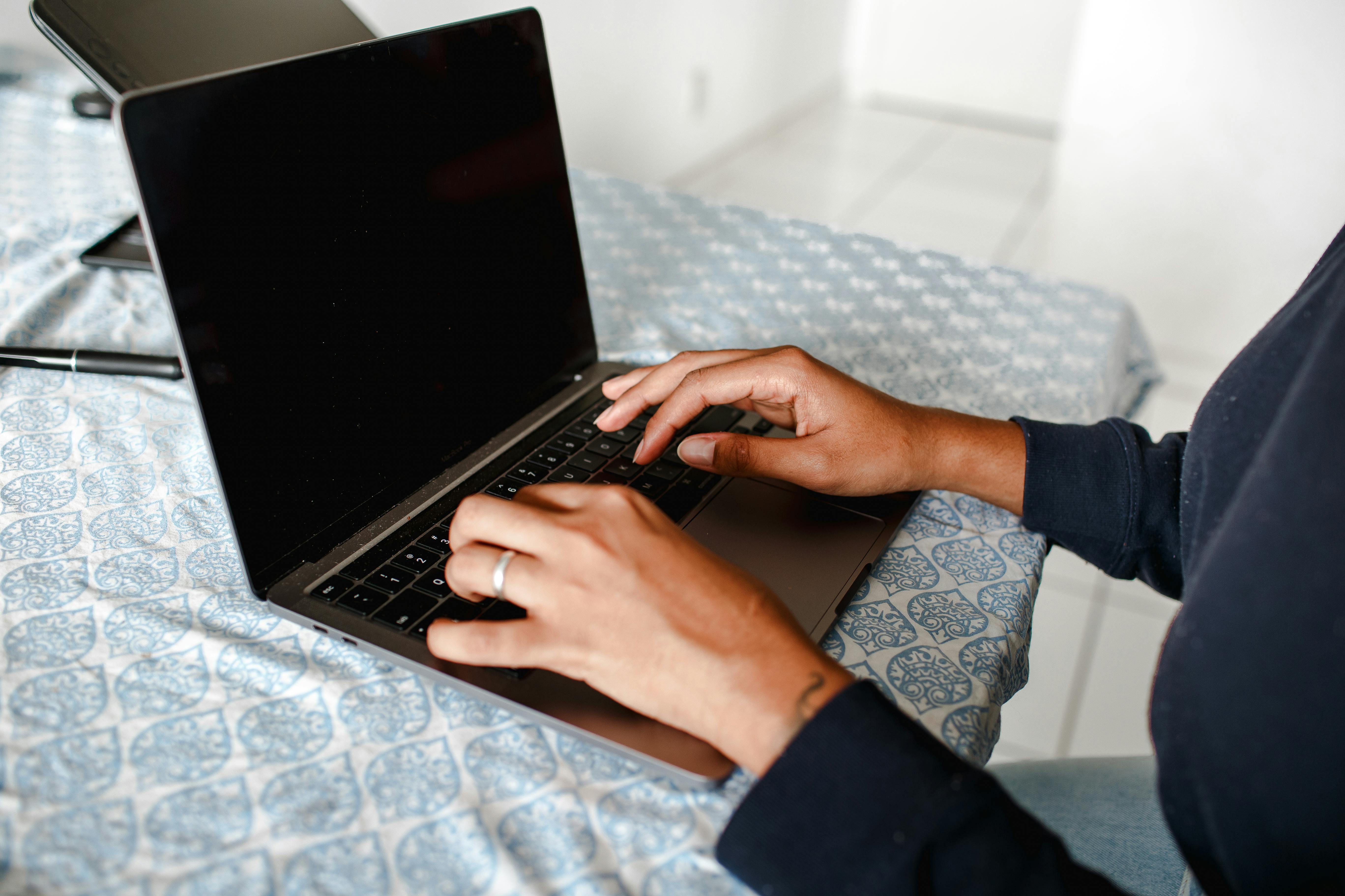 Person typing on the keyboard of a laptop on a table with a light blue table cloth.