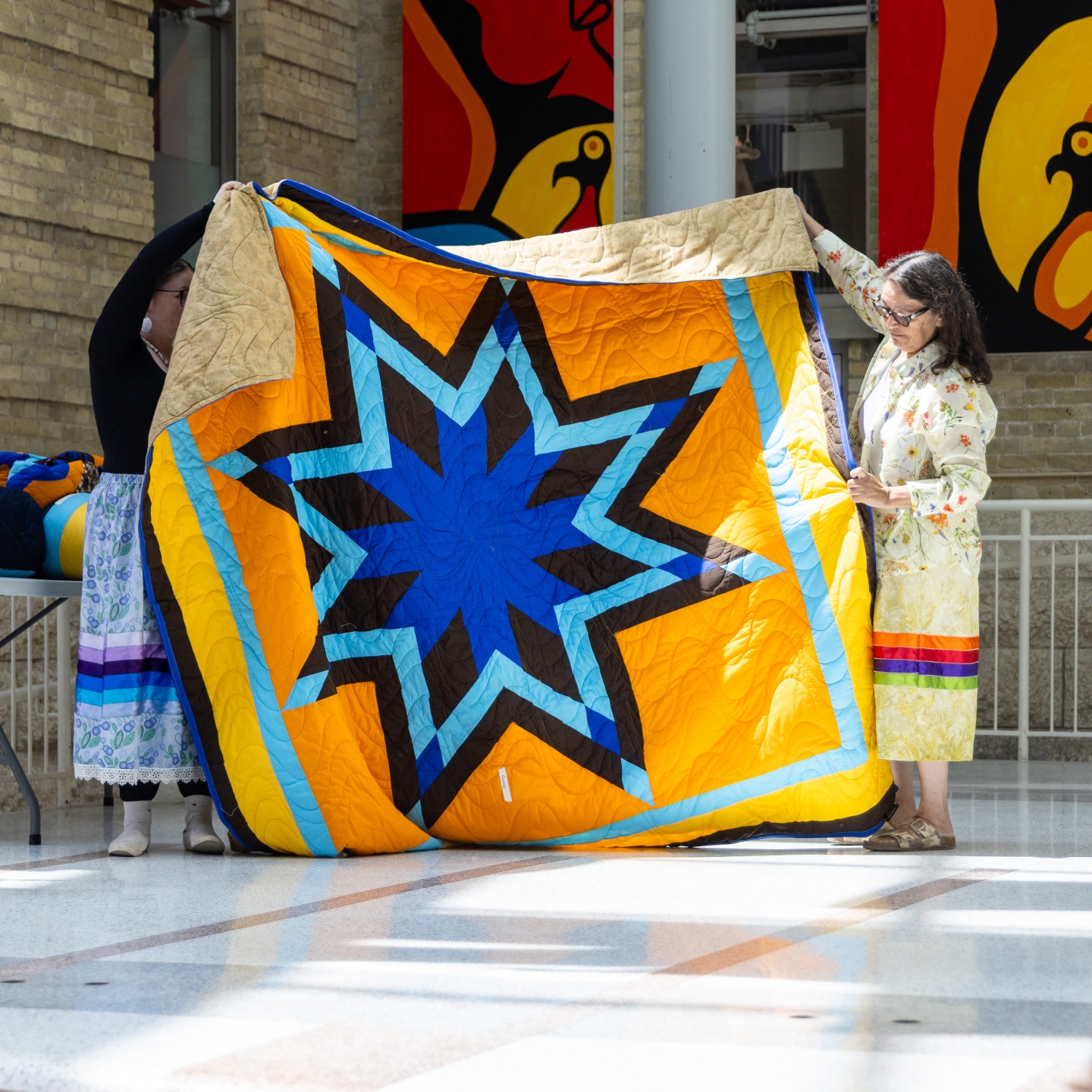 golden yellow and blue star blanket held by two women, being presented.