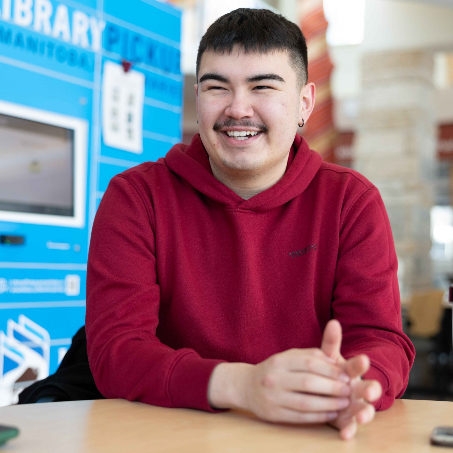Male smiles candidly, seated at table wearing a red sweater.