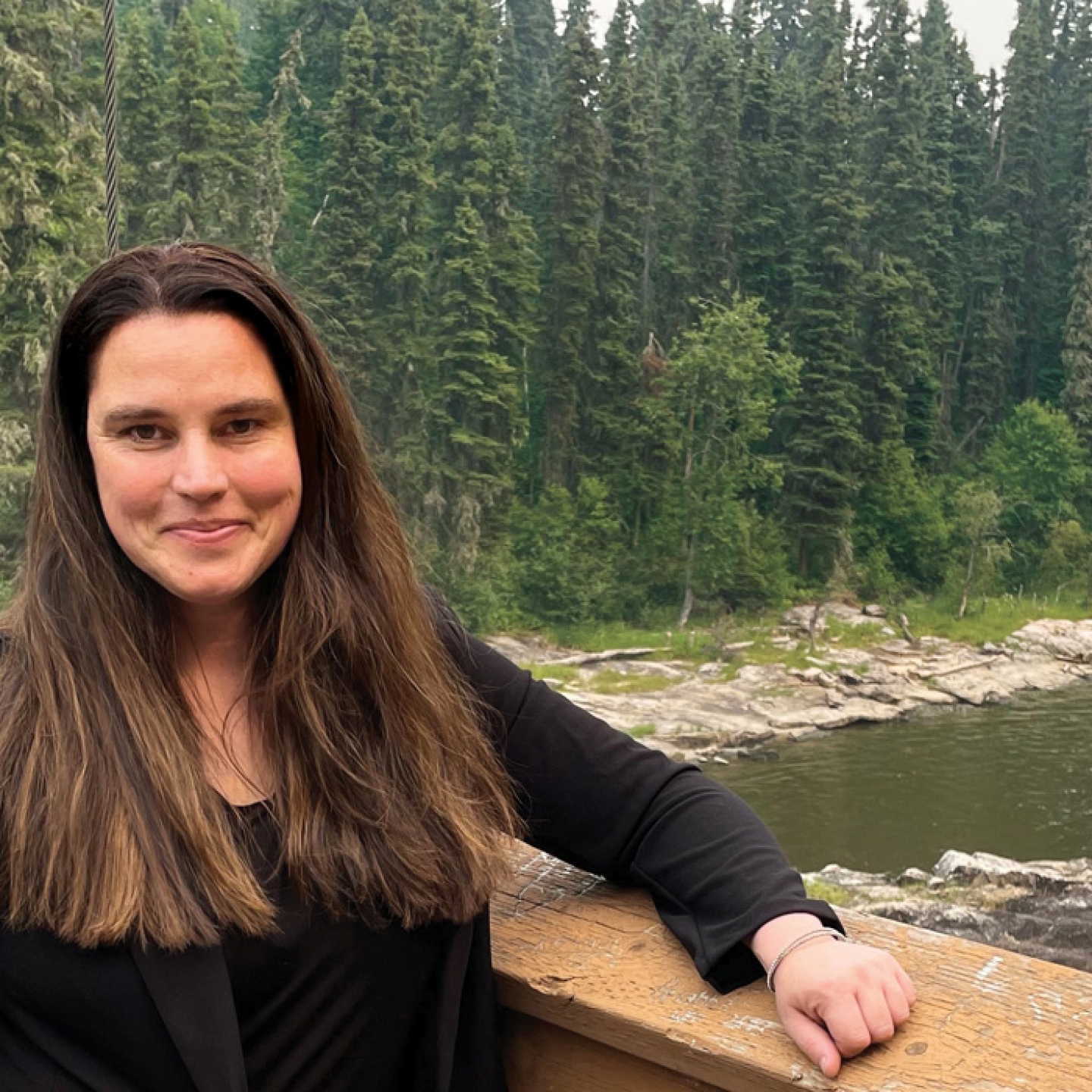 Cherie Murie stands on a bridge with a forest behind her.