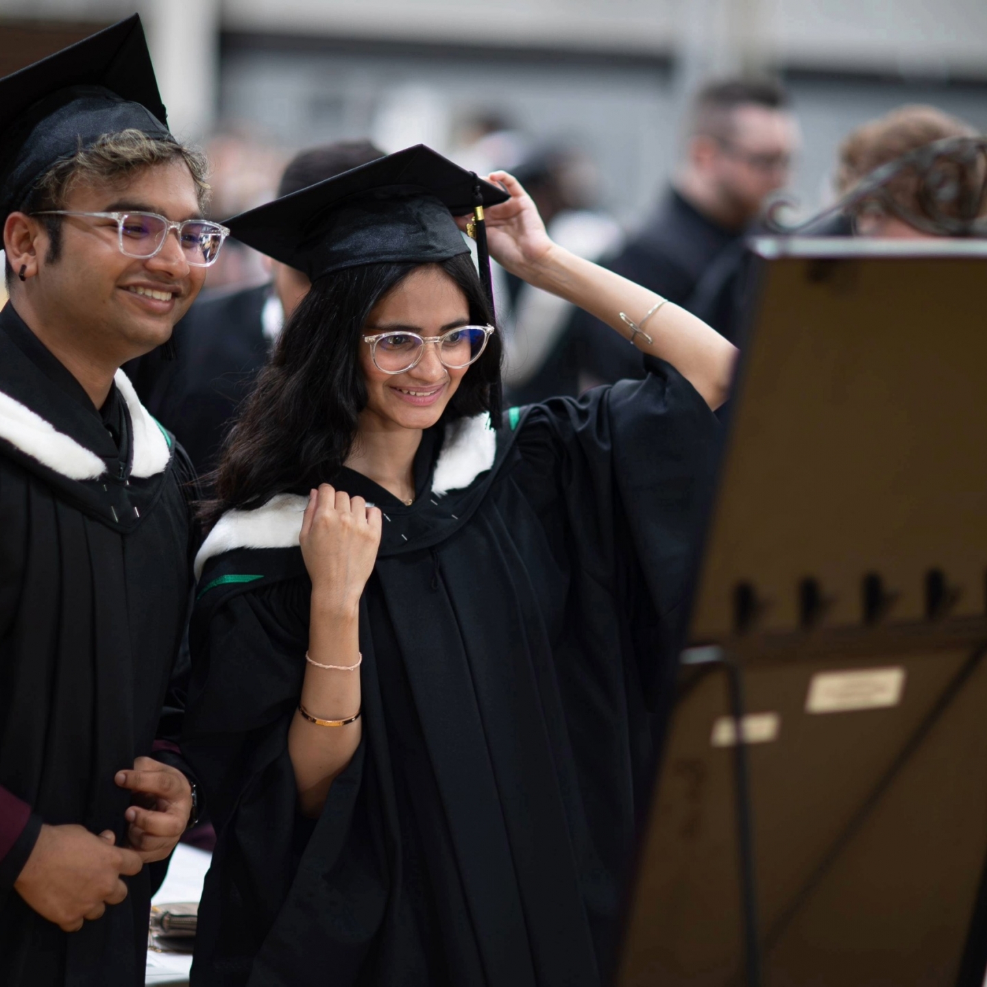 Two graduands looking in the mirror while getting ready at Convocation.