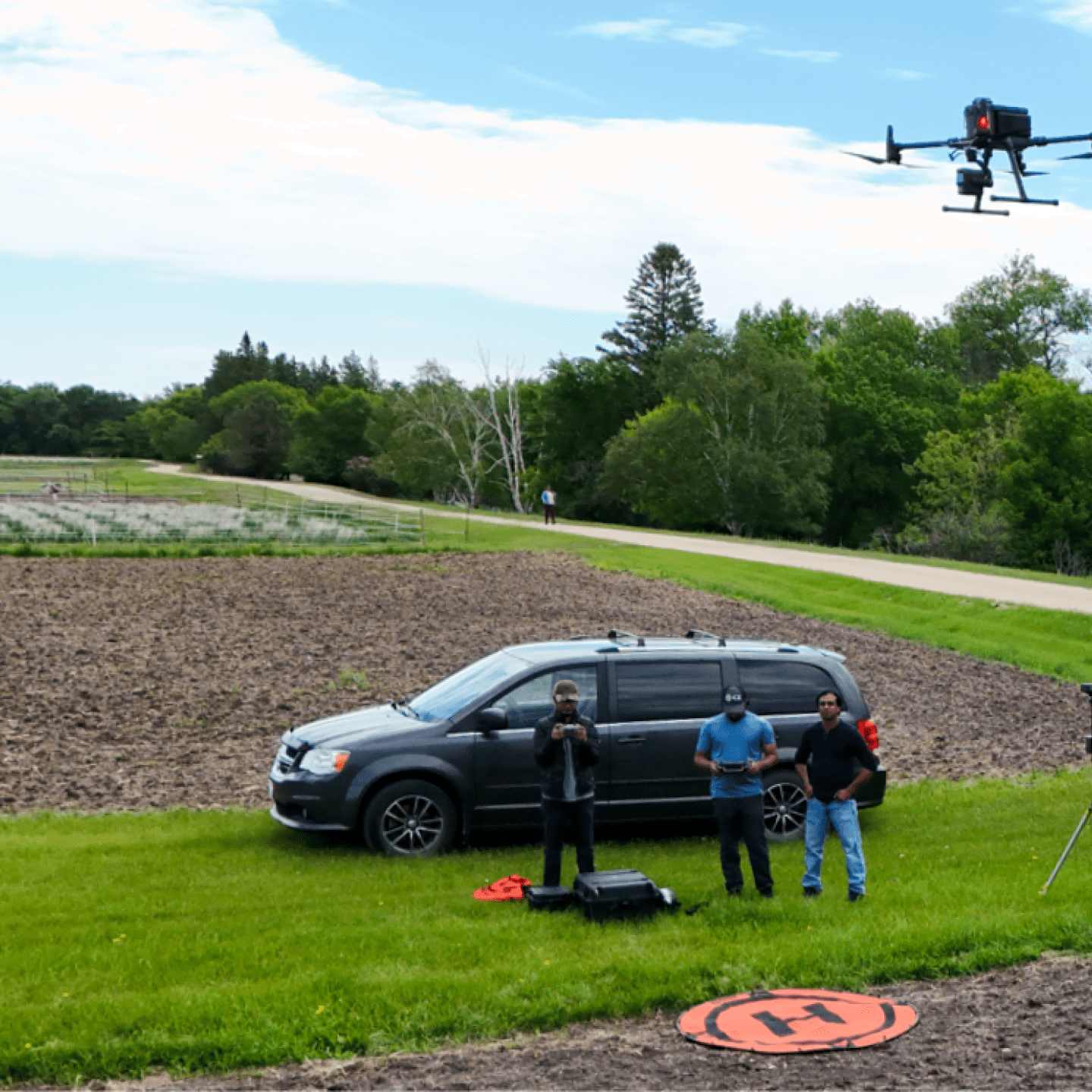 Three men stand outside in a field in front of a van.