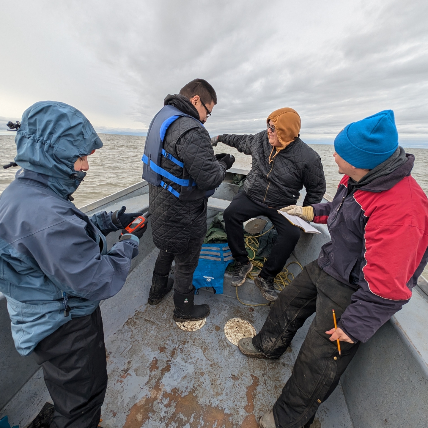 four people on a small boat looking at water samples 