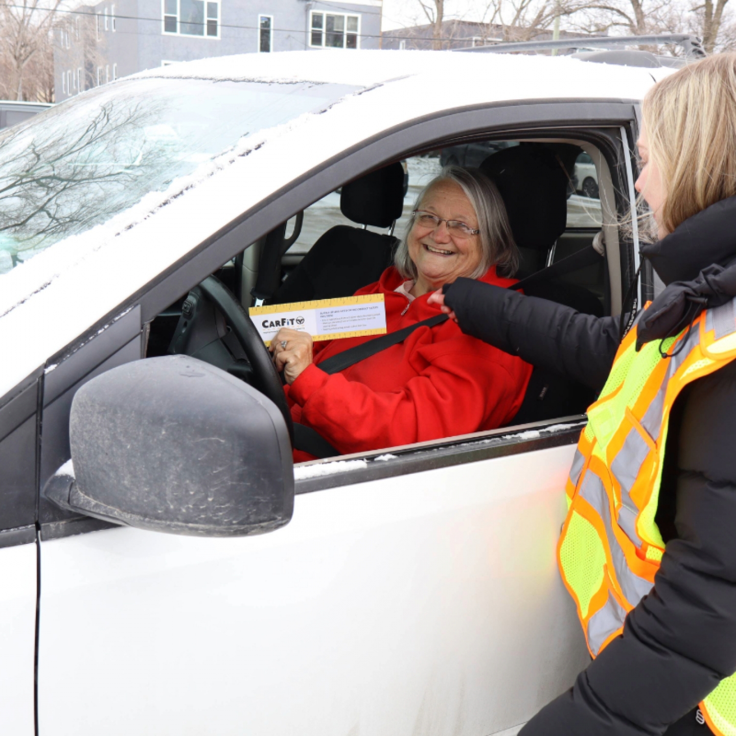 A student volunteer does safety measurements with an older driver in her car.