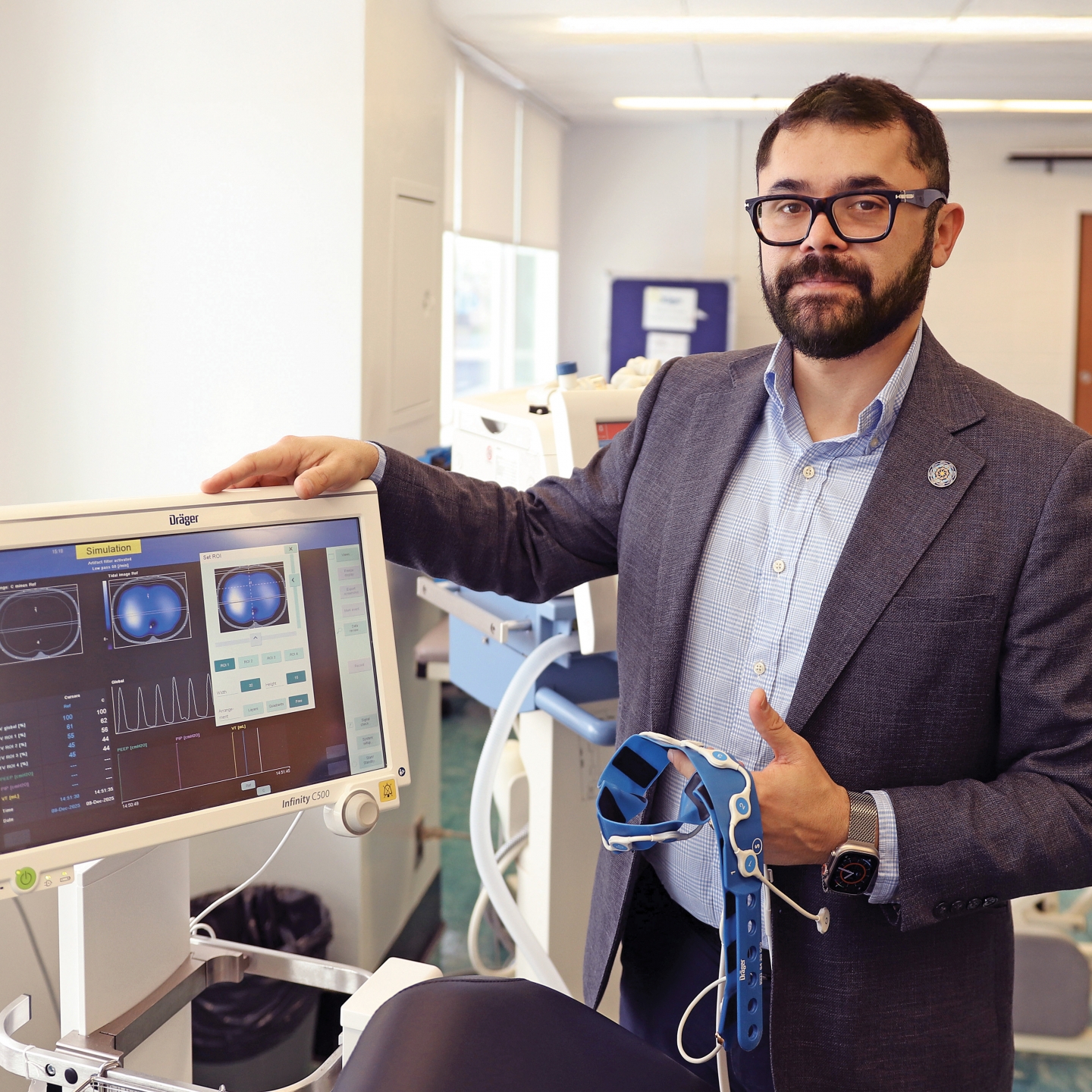 Mayson Sousa stands next to ventilation machine in a lab setting.