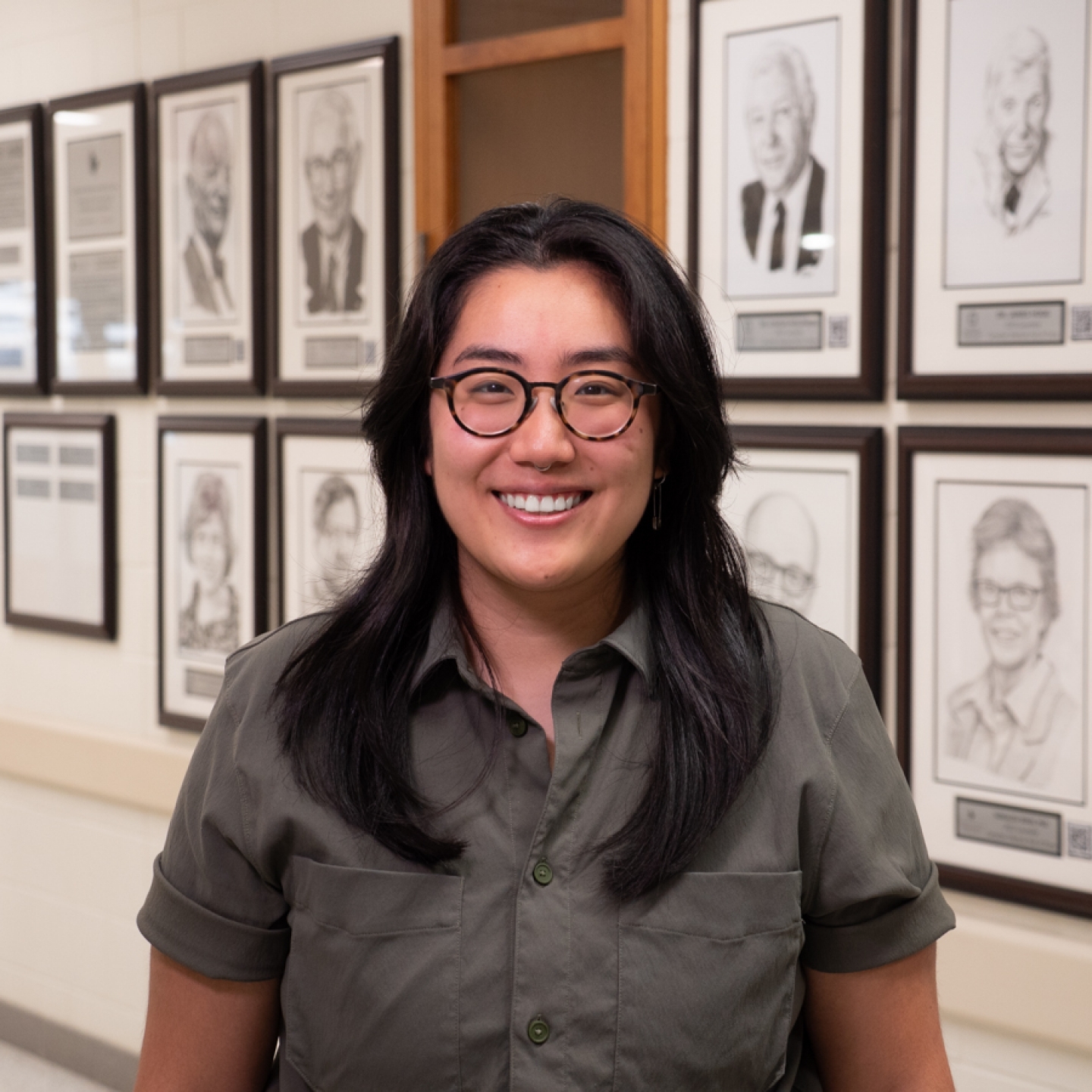 A person standing in front of a wall with framed photos of ten people.