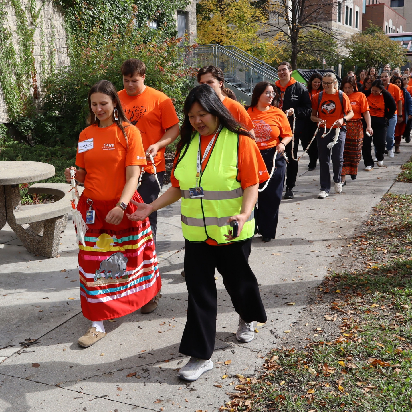 A group of people in orange shirts walking on the sidewalk.