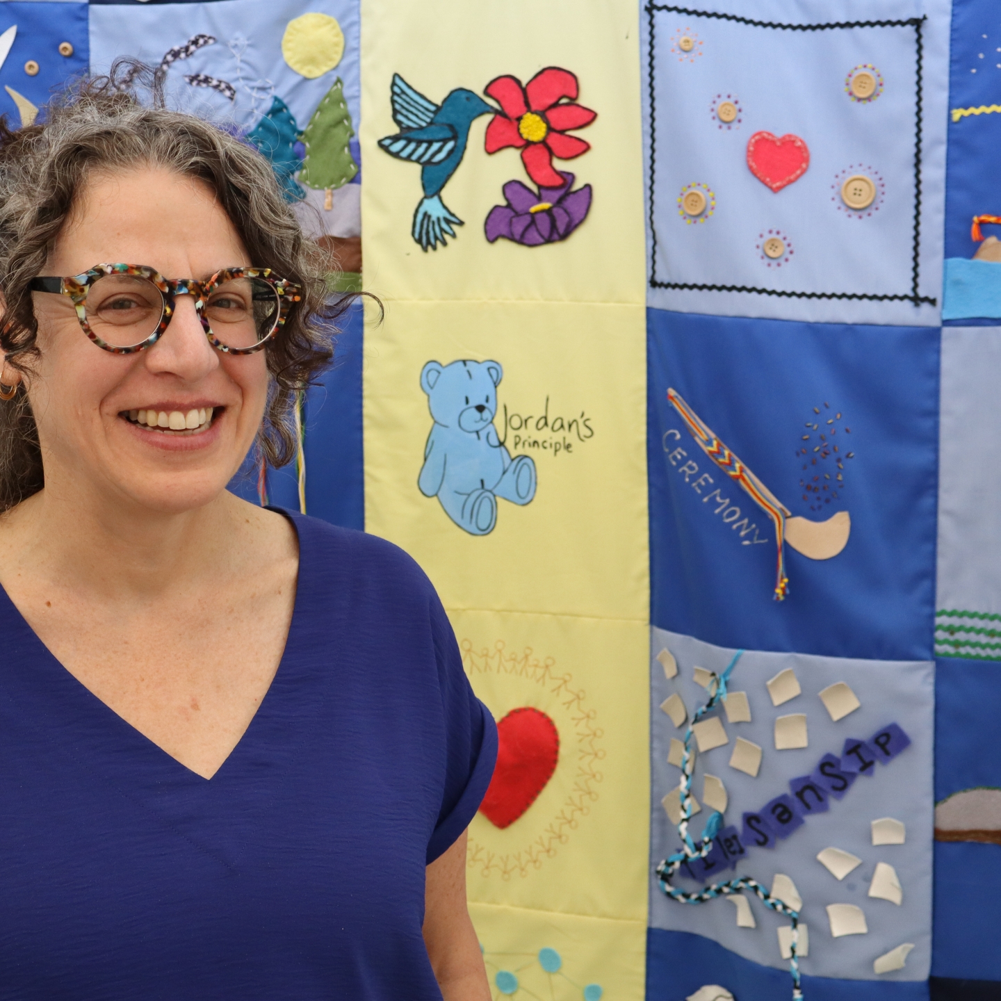 Pam Becker stands next to a quilt that features a Jordan's Principle logo.