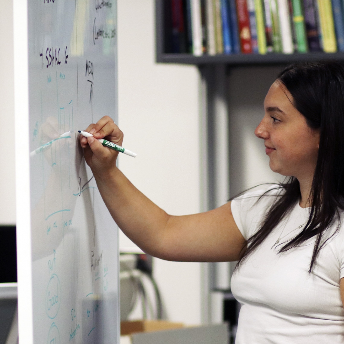 A young researcher writes on a whiteboard.