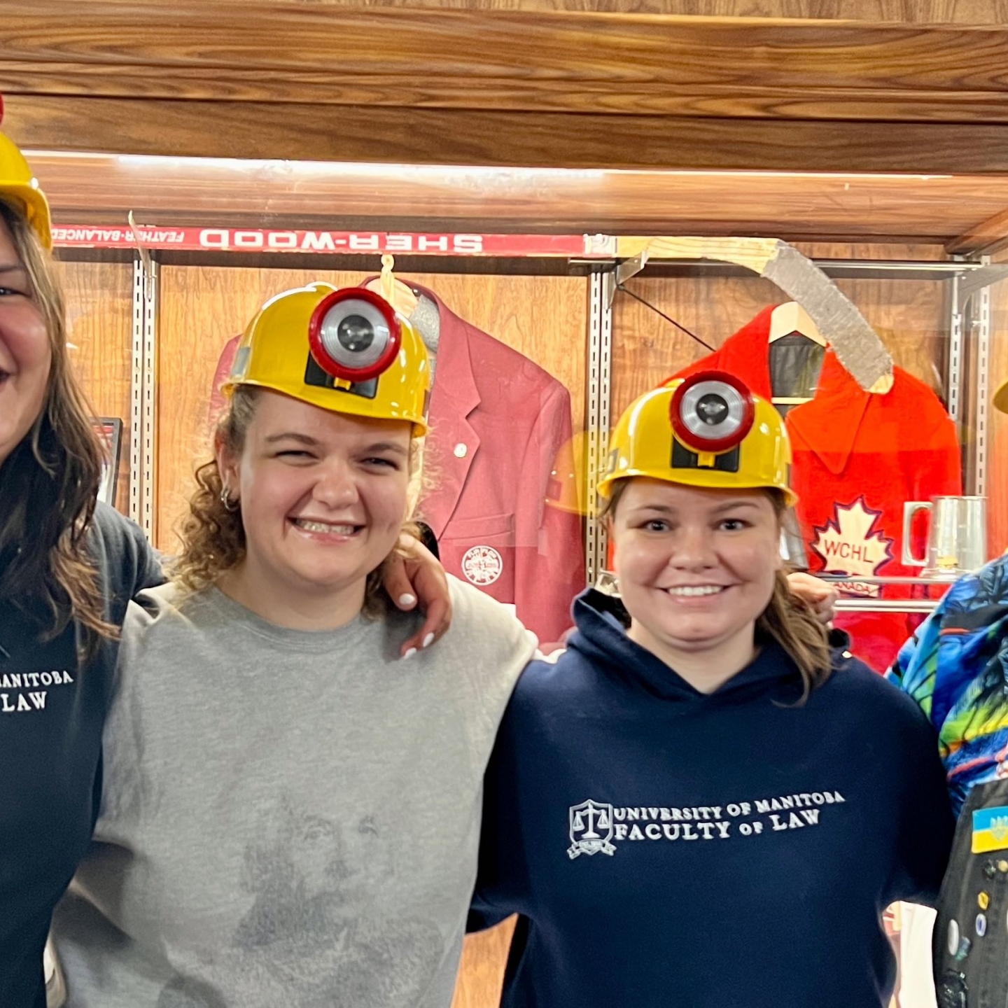 three women and one man in yellow miner hats smile together