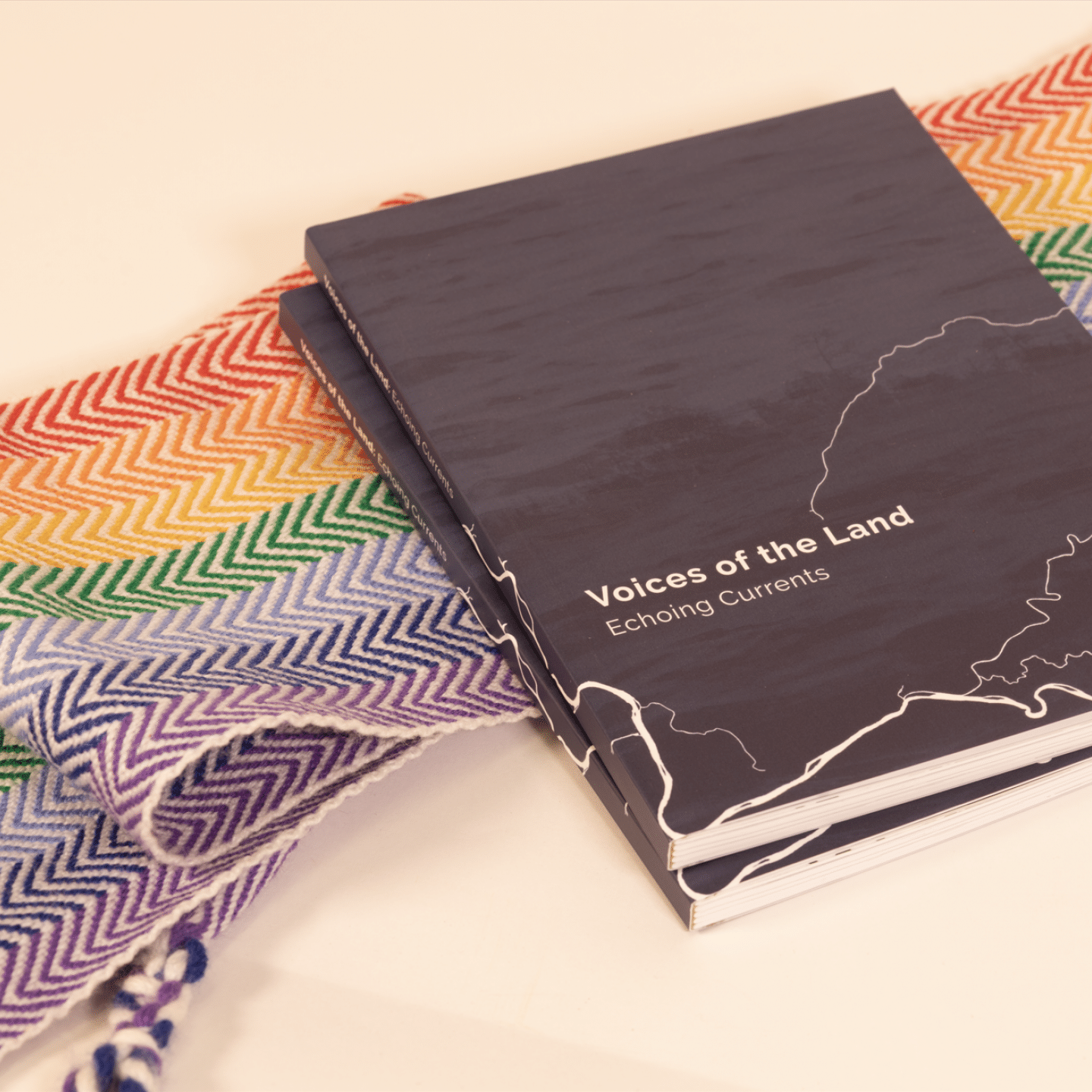 Dark book titled “Voices of the Land: Echium Currents” rests on a colorful woven textile, creating a calm, artistic scene.