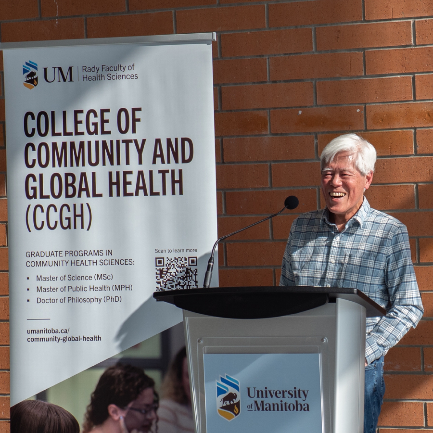A person stands behind a podium smiling. Beside him is a College of Community and Global Health banner.