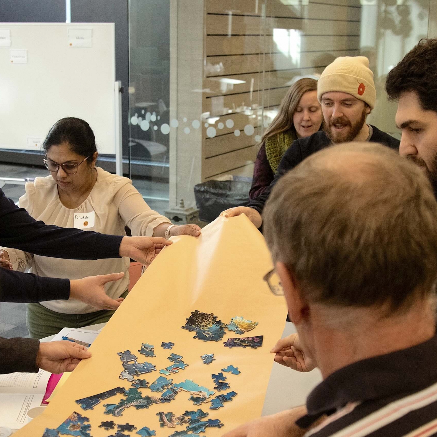People hold a large piece of tan-coloured paper topped with bright blue puzzle pieces.