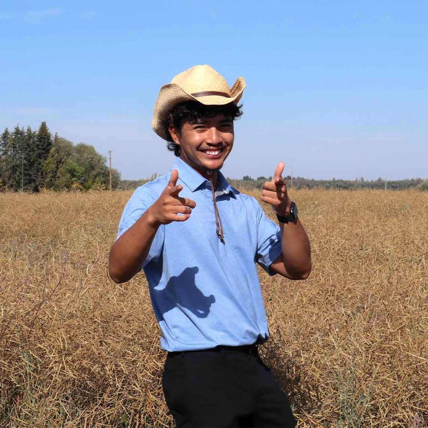 Brigo wearing a blue collared shirt with a hat smiling at the camera.