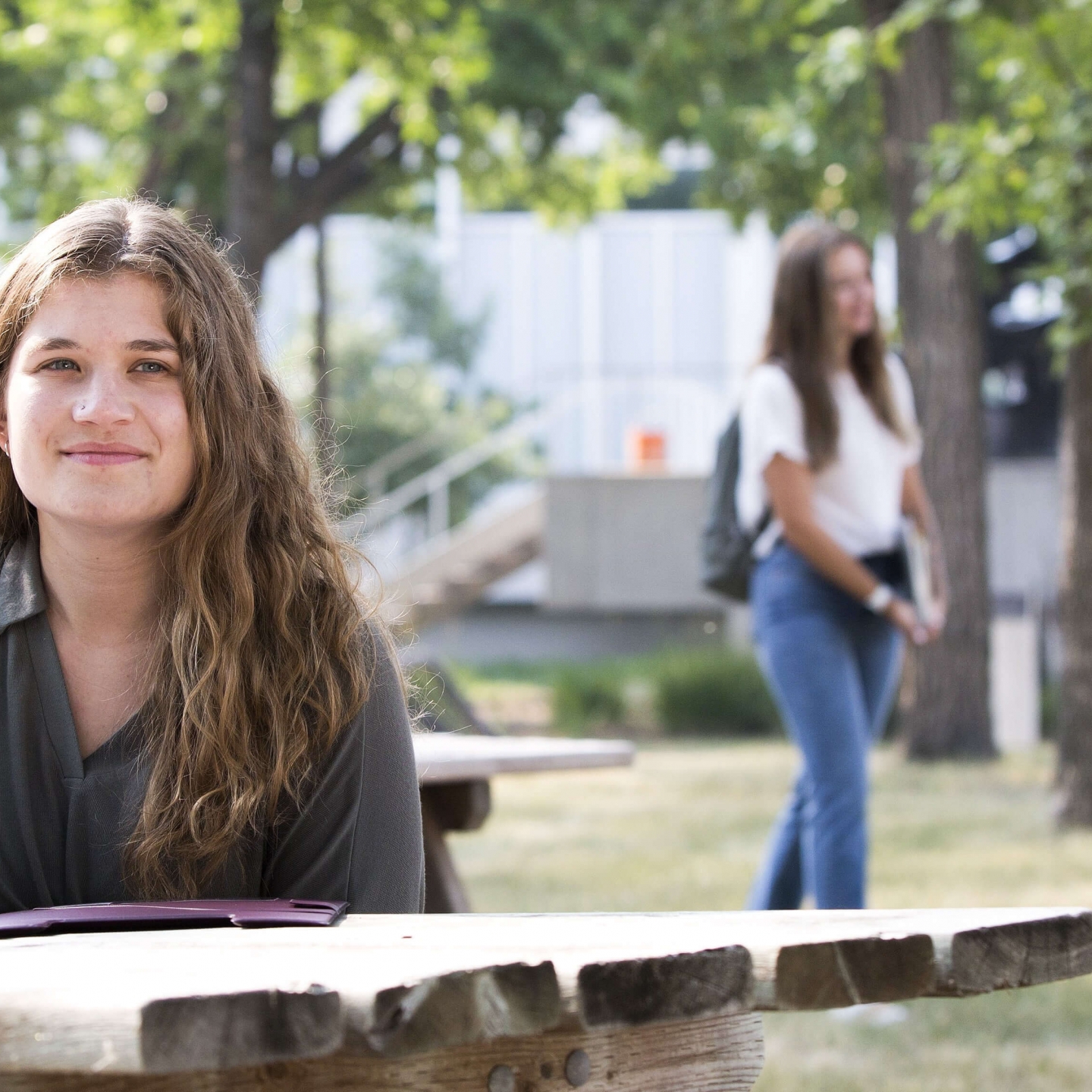 Smiling young woman sits outdoors at picnic table at Fort Garry campus.