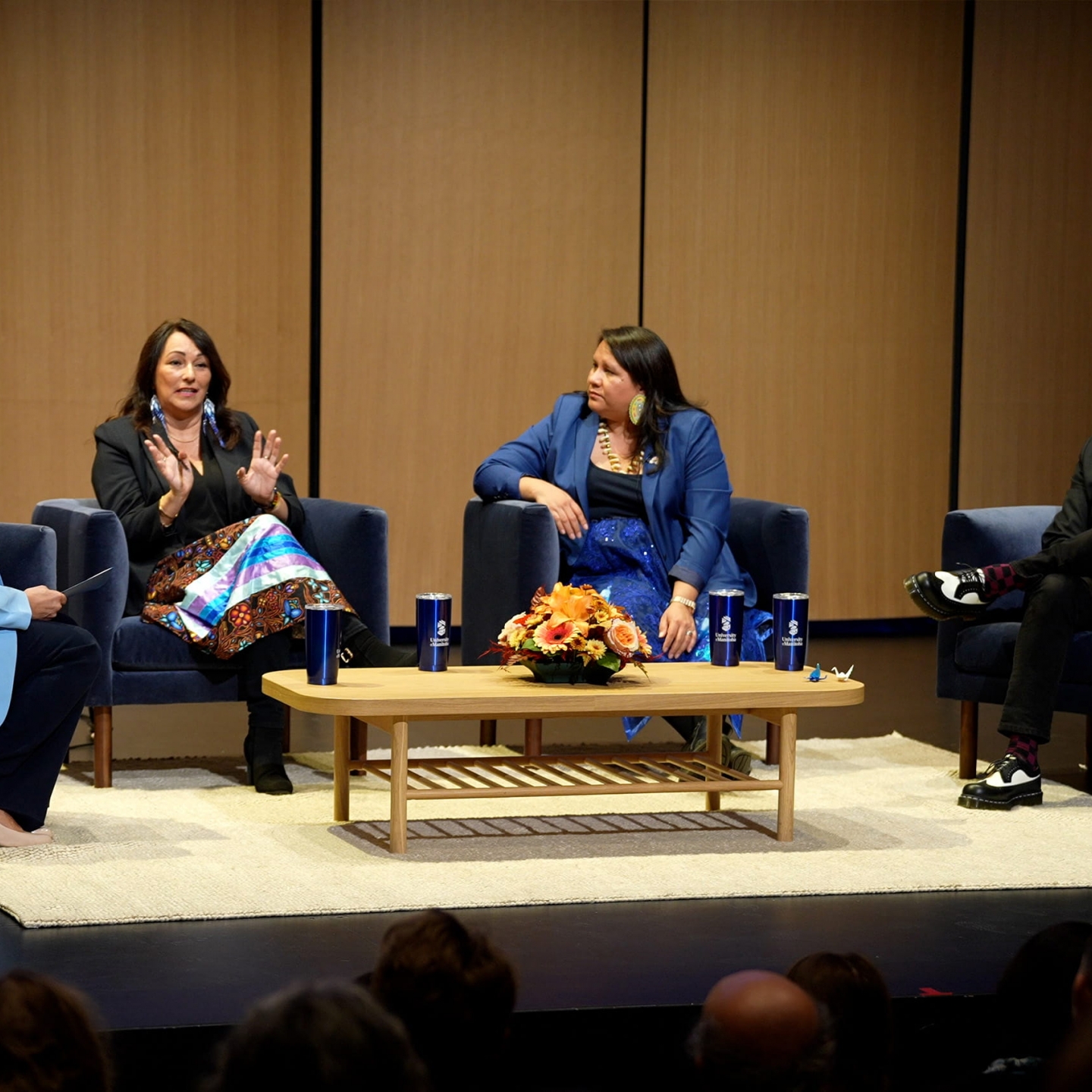 Angie Bruce, Diane Roussin, Kathleen Bluesky and Peter Pomart in conversation seated in chairs on a stage around a coffee table.