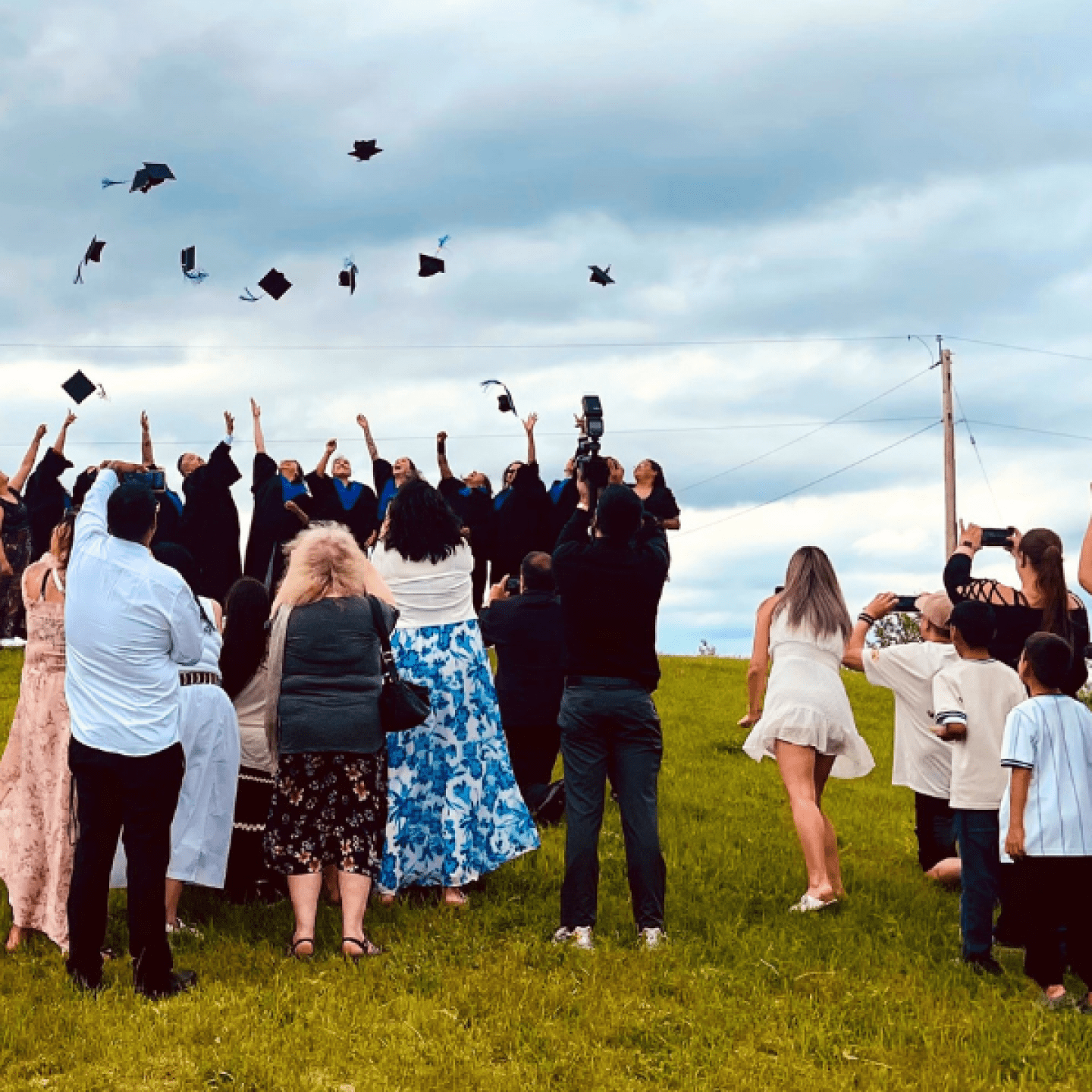 Graduates toss their caps as family and friends celebrate outdoors.