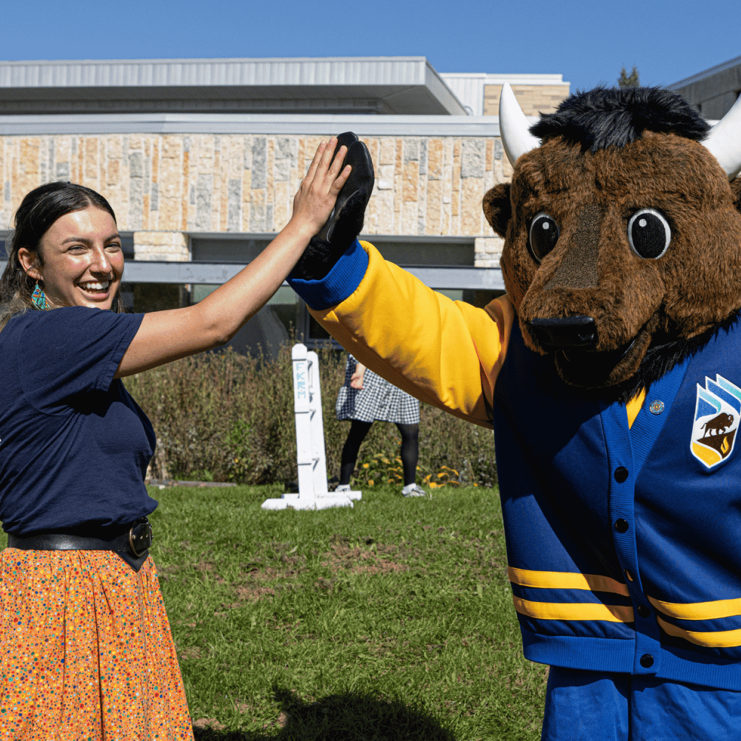 An Indigenous student high-fives the Bisons mascot outdoors.