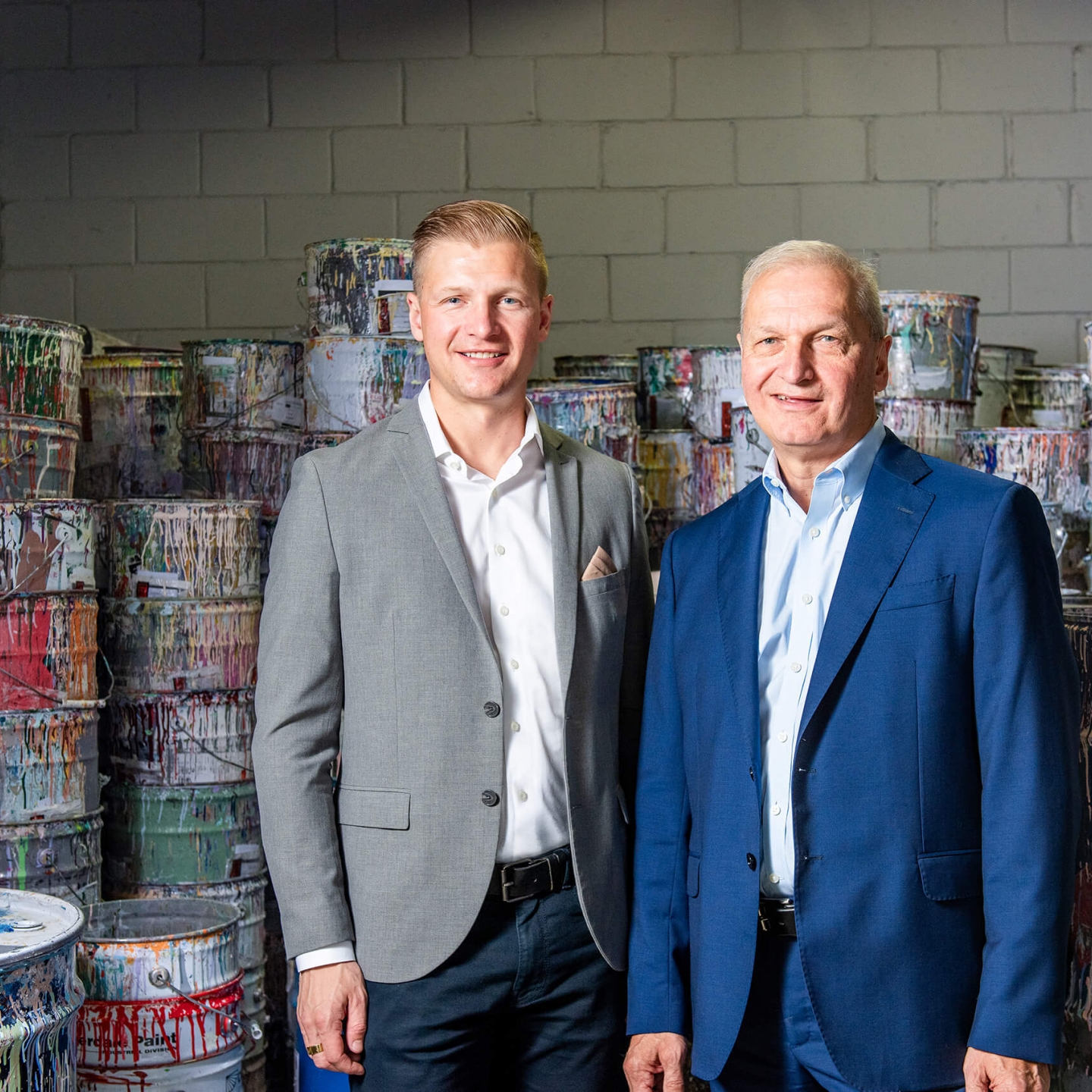 Two men standing in front of large paint cans