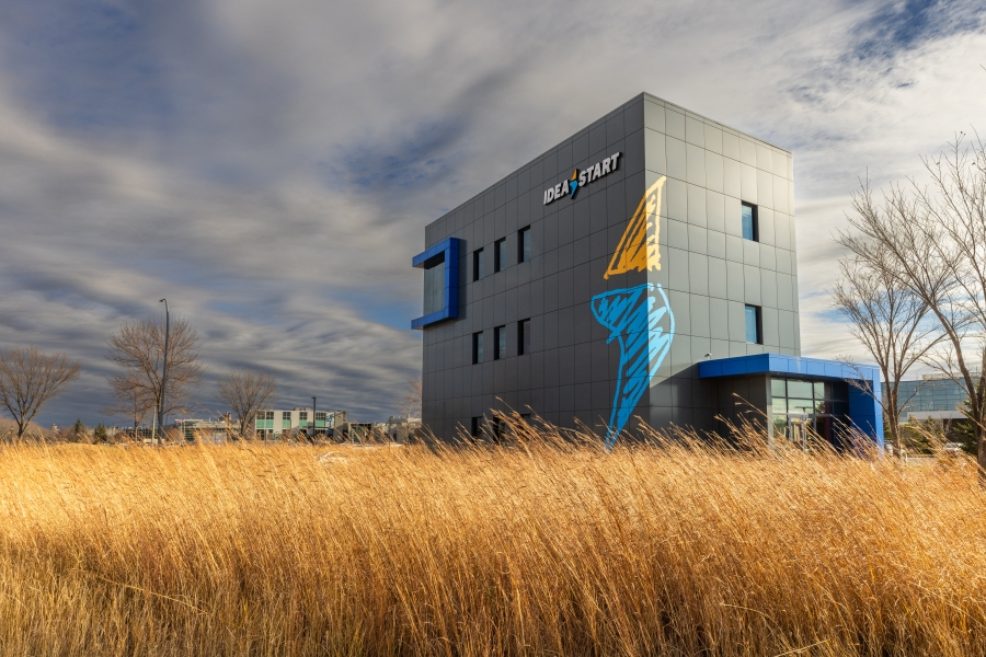 IDEA START building at the University of Manitoba, set against prairie grass and a cloudy sky