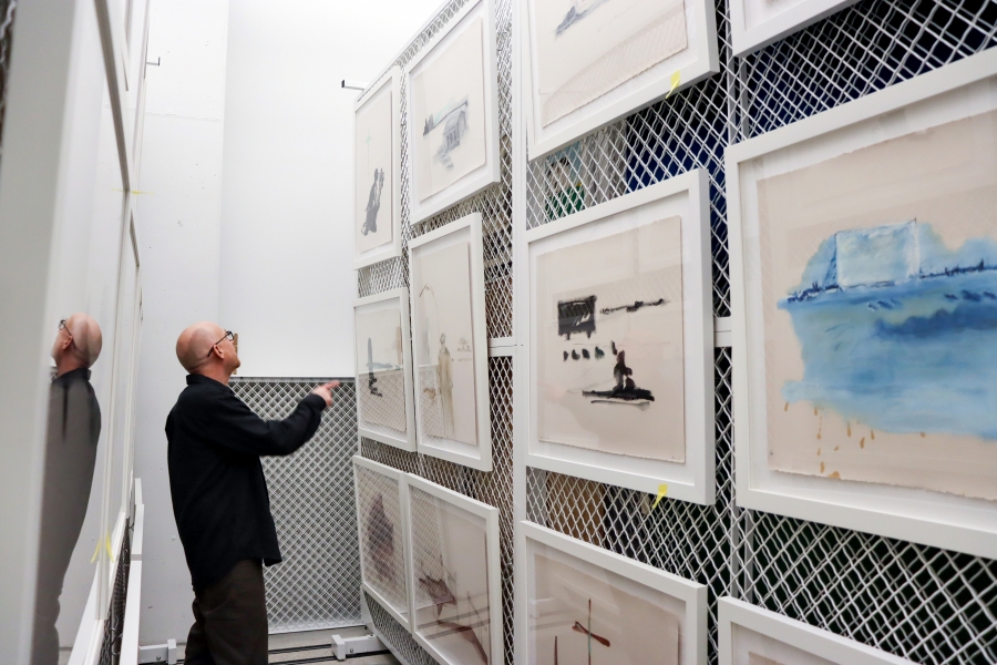 Derek Dunlop points up while viewing framed works on mesh storage racks in the School of Art Gallery.